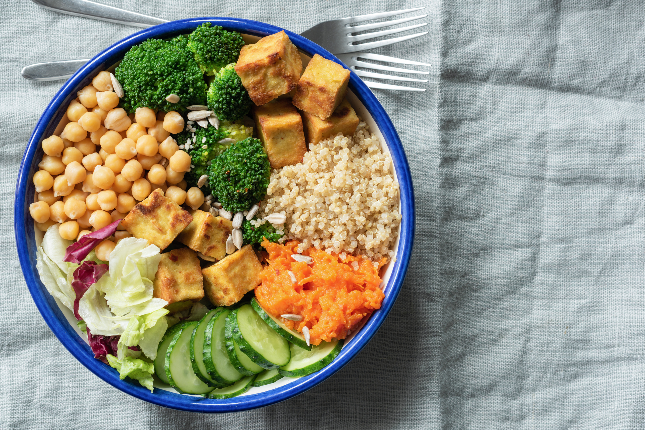 High-protein salad bowl with quinoa, tofu, chickpeas and vegetables on linen textile background.
